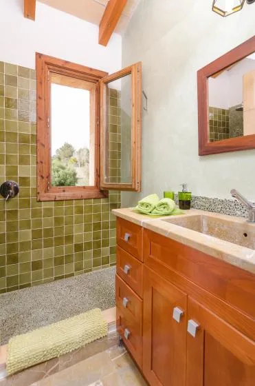 A tiled bathroom with a wooden vanity, sink, and open window.