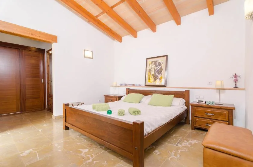 A bedroom with a wooden bed beneath exposed ceiling beams.