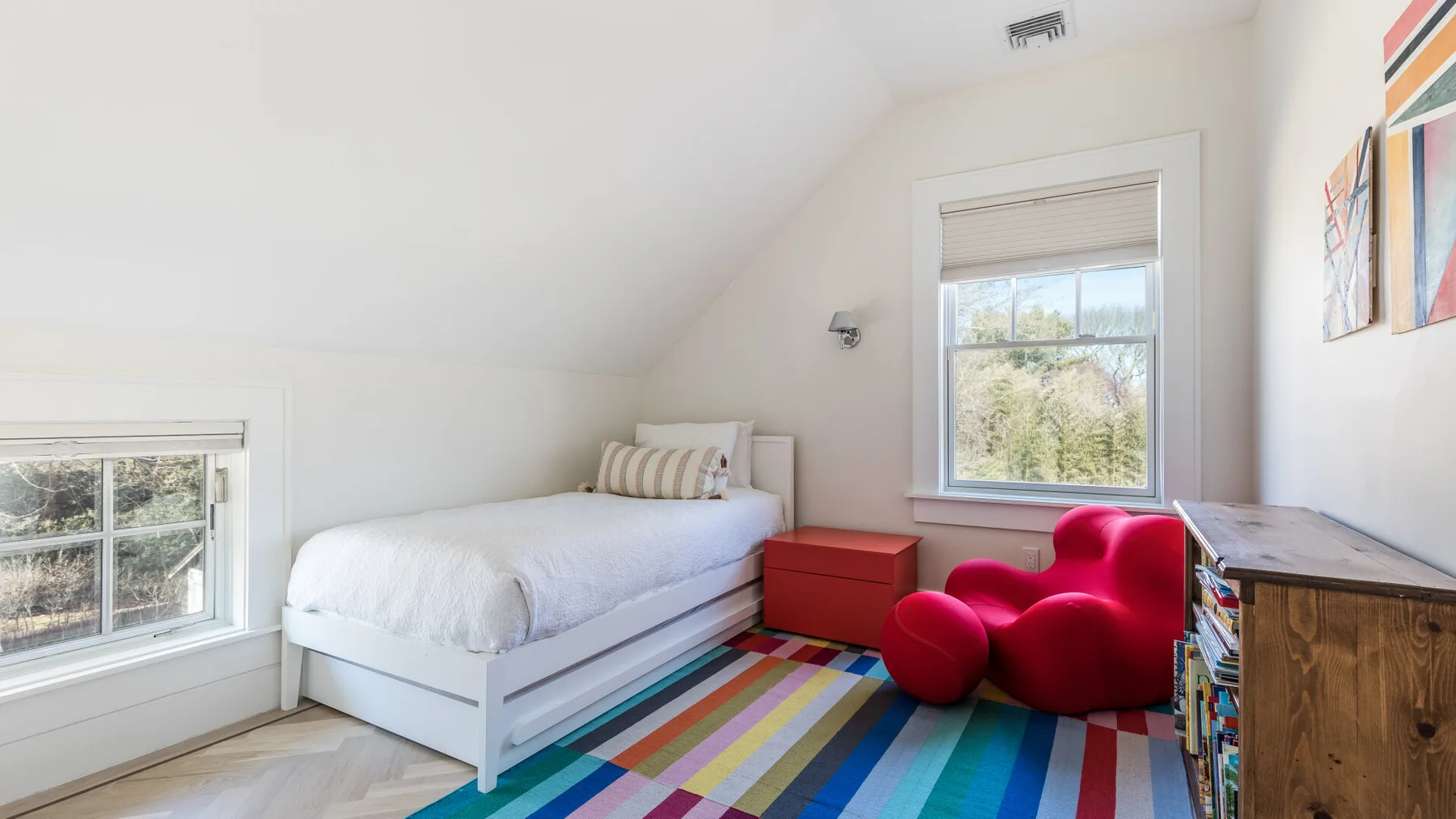 A bright bedroom with a white bed, colorful rug, and red seating.
