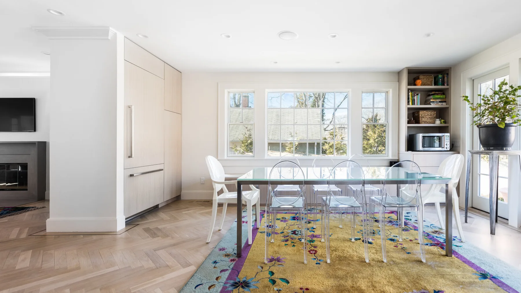 A bright dining area features a glass table beside large windows.
