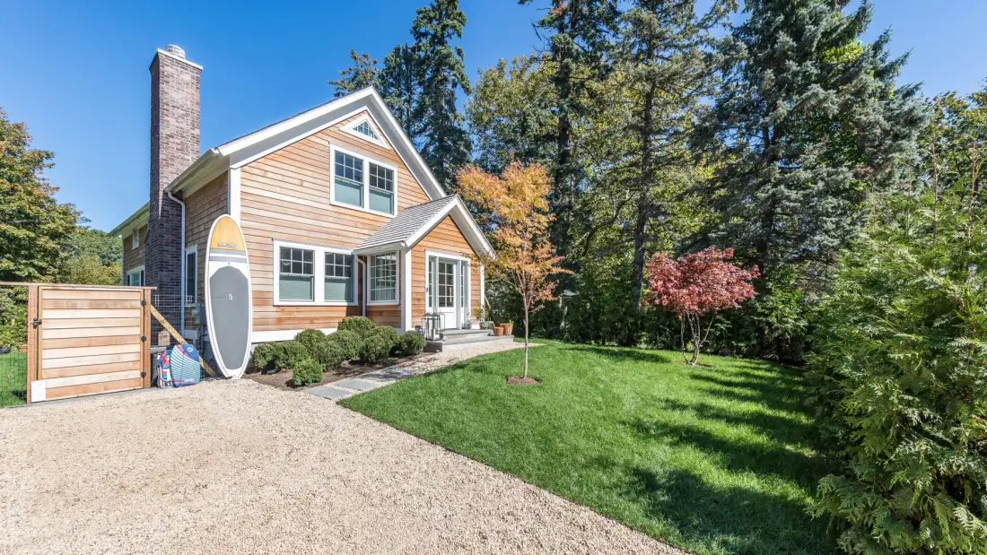 A two-story house stands beside a gravel driveway and a green lawn.