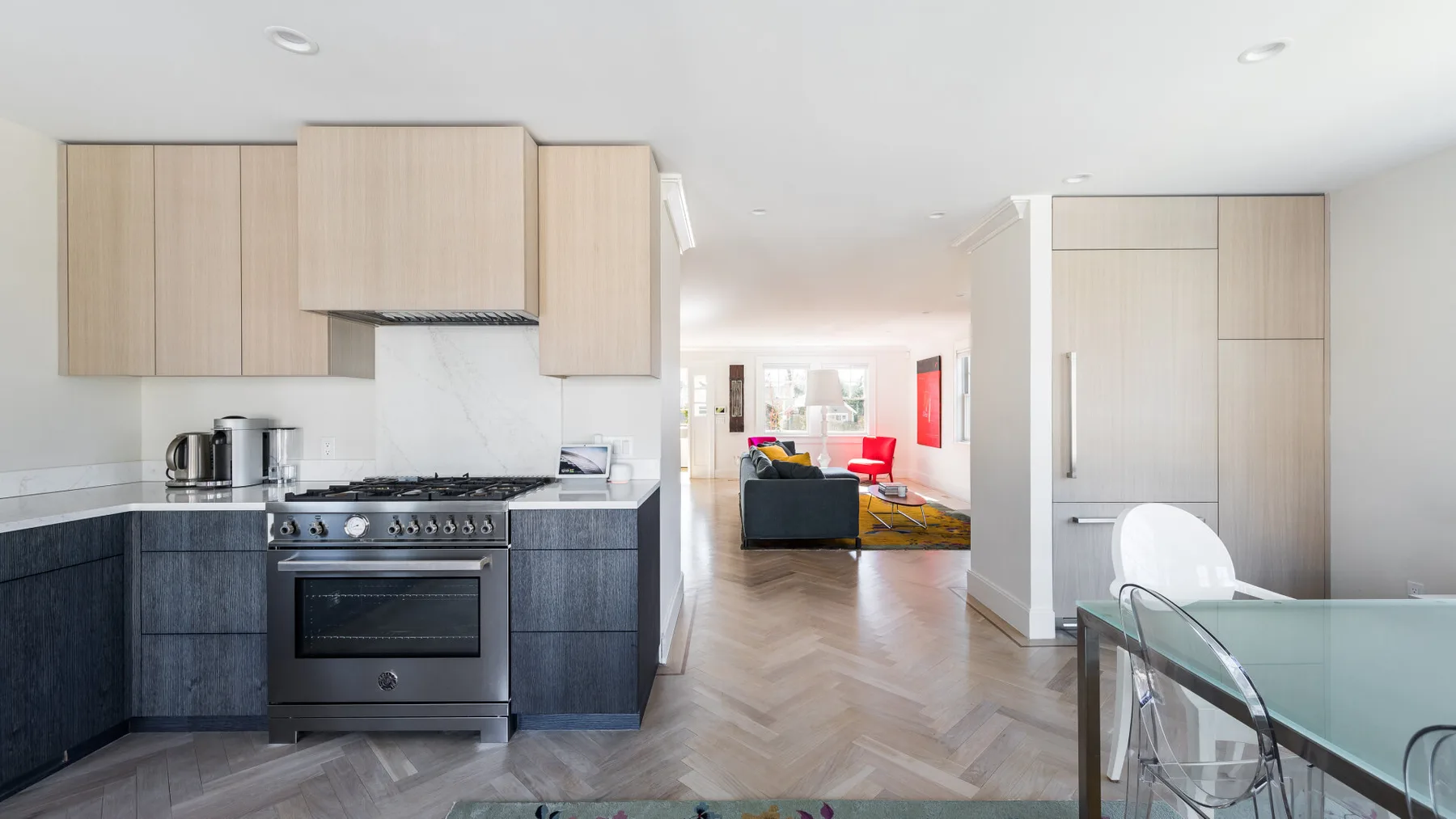 Una cocina y comedor de concepto abierto con gabinetes de madera clara y una mesa de vidrio.