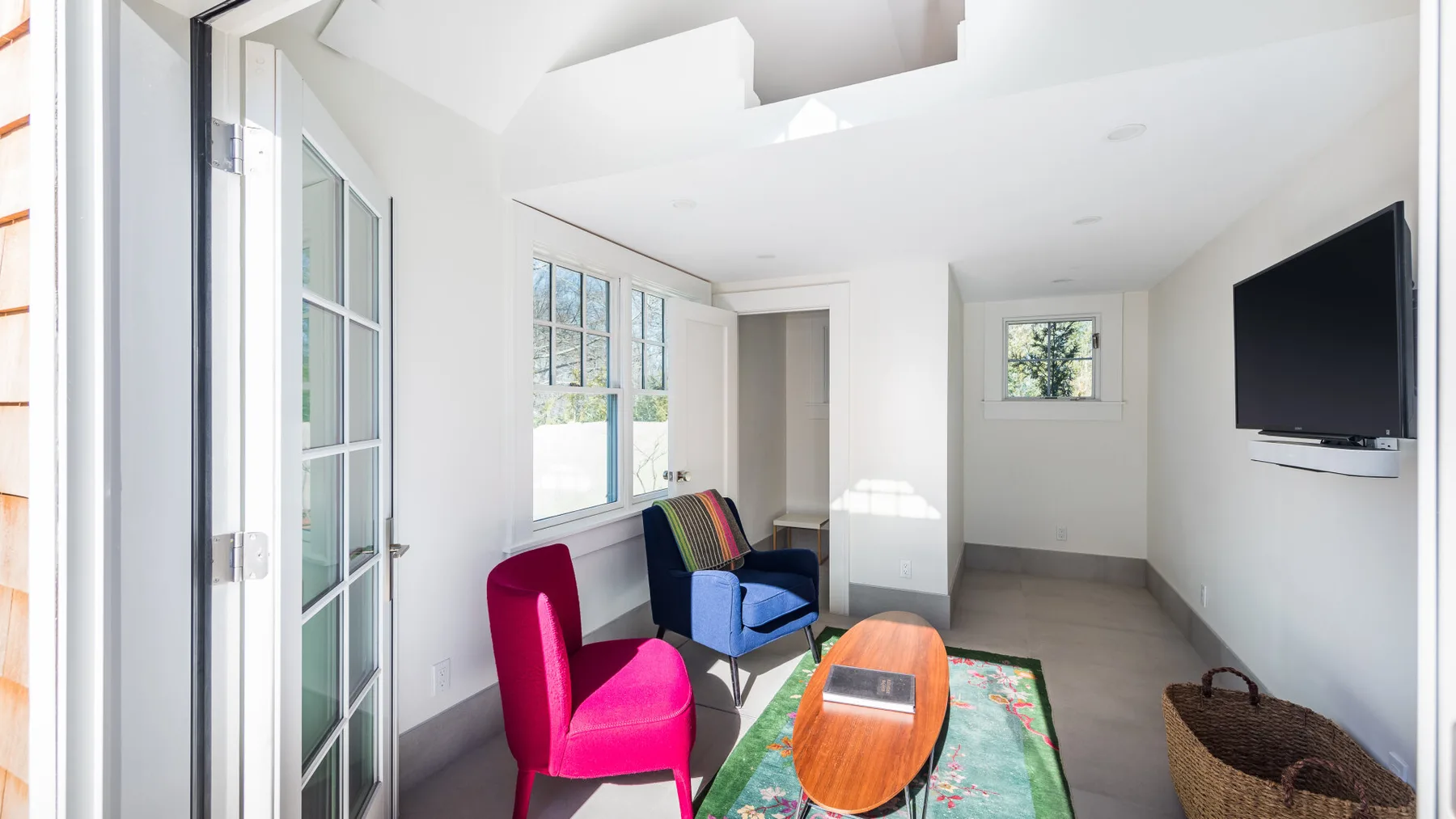 A bright living room has colorful seating, a low table, and a wall-mounted television.
