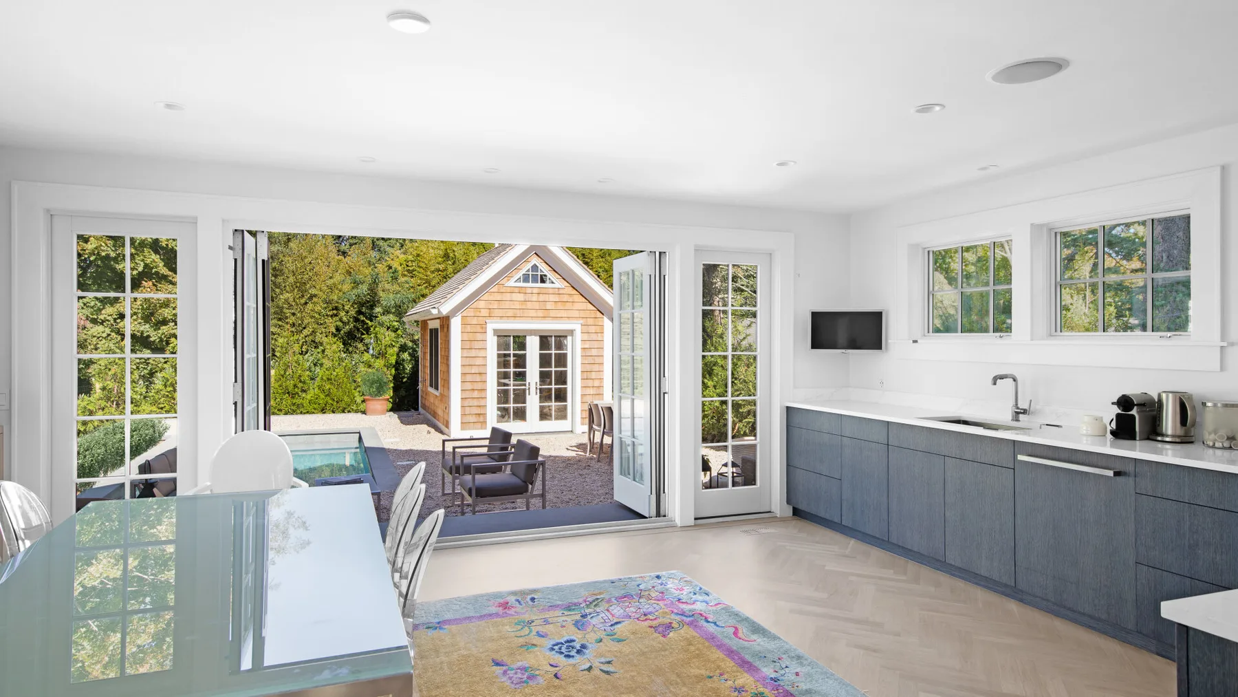 A bright kitchen and dining area opens onto a patio with a small garden building.