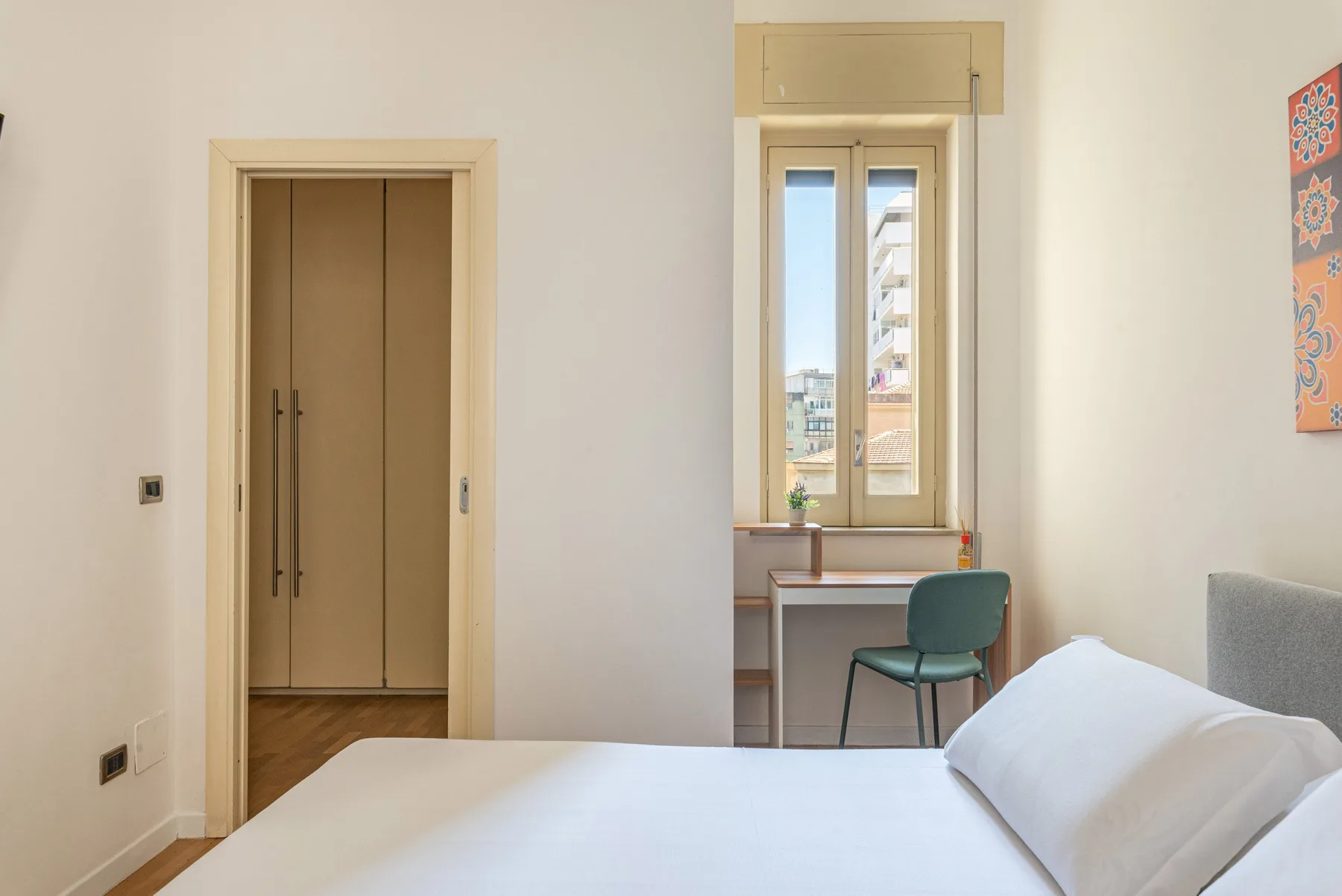 Un dormitorio con una cama y un escritorio junto a una ventana alta.