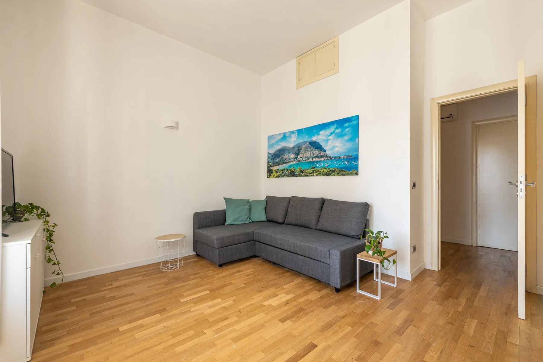 A living room with a gray sectional sofa and a colorful landscape picture on the wall.