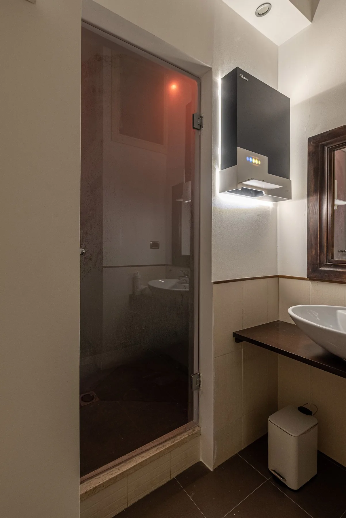 Un baño con una ducha de vidrio y un lavabo junto a una encimera oscura.