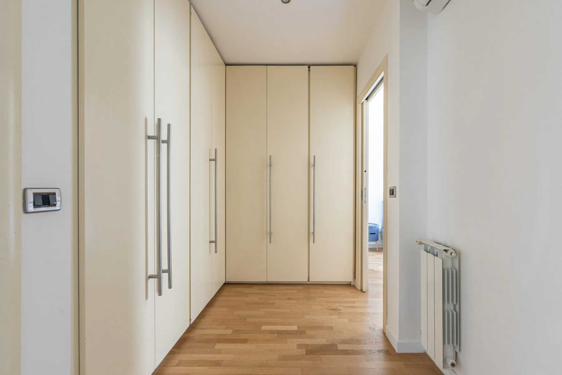 Un pasillo interior luminoso con armarios empotrados y suelo de madera.