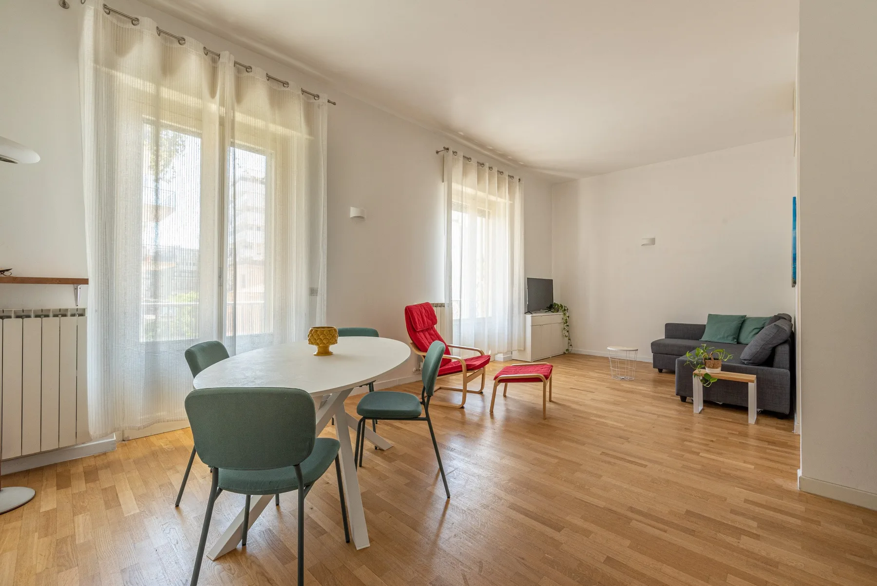 Un salón-comedor luminoso con una mesa, asientos y grandes ventanas con cortinas.