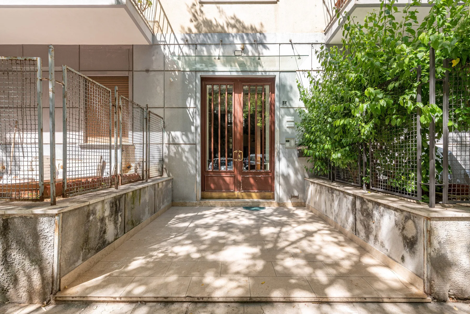 Un camino exterior pavimentado conduce a una puerta de madera con barrotes, junto a la vegetación.