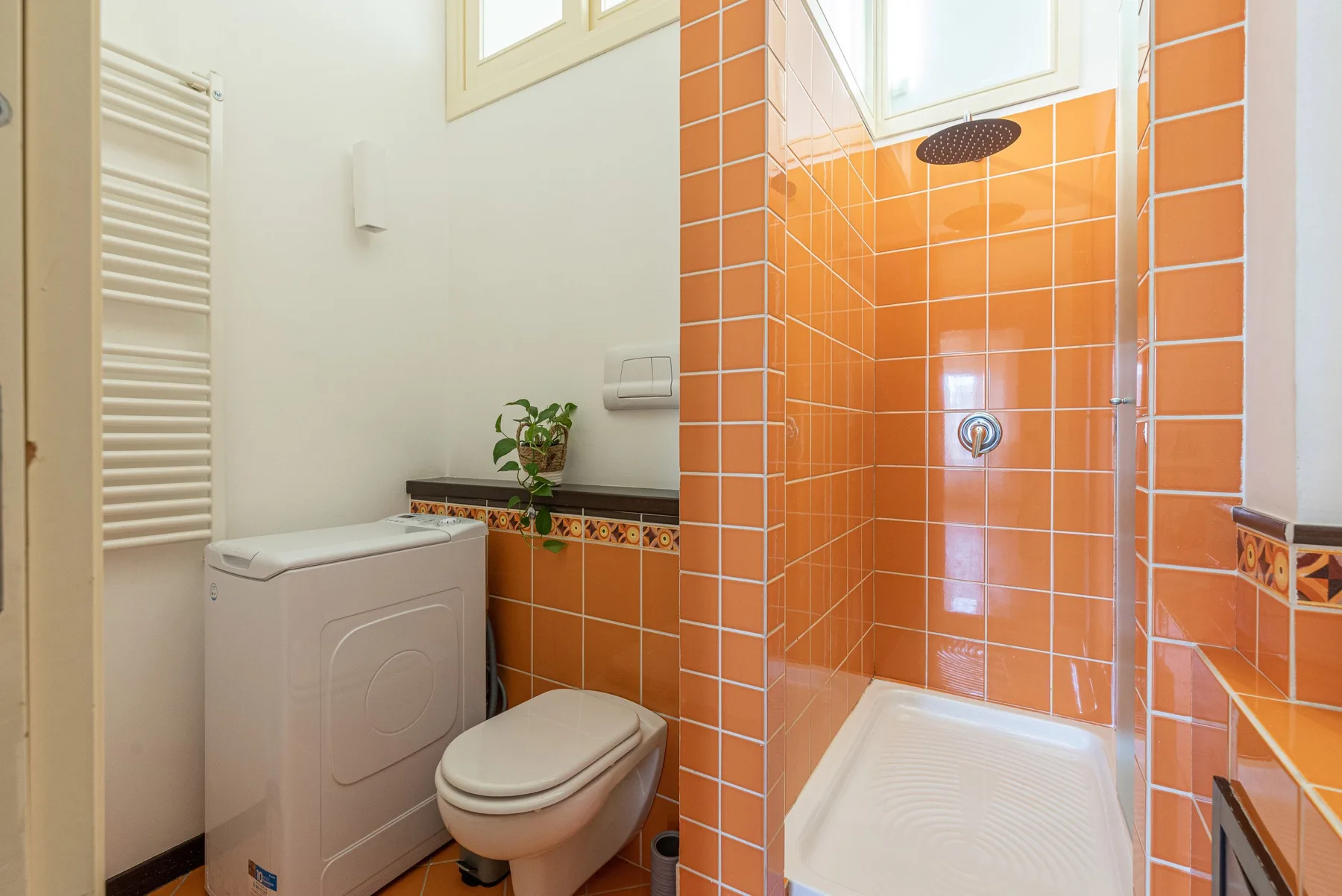 Un baño con azulejos, ducha, inodoro y lavadora.