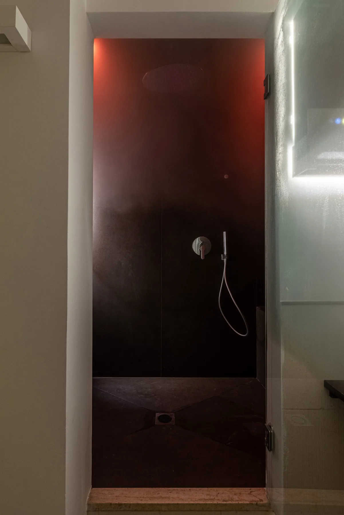 Una zona de ducha oscura con ducha de mano y desagüe en el suelo.