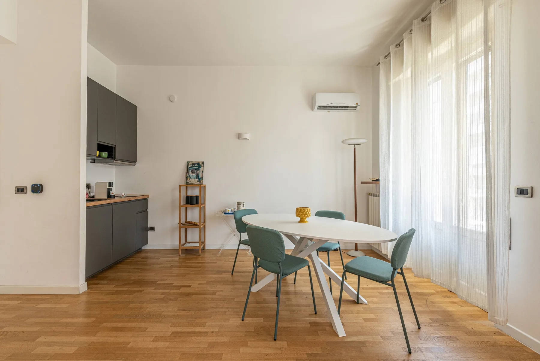 Un comedor luminoso con una mesa blanca y asientos verdes junto a ventanales con cortinas.