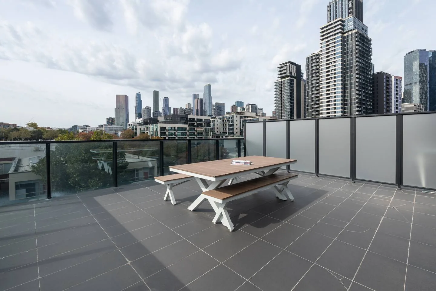 A rooftop terrace overlooks the city skyline, with a picnic table on the tiled deck.