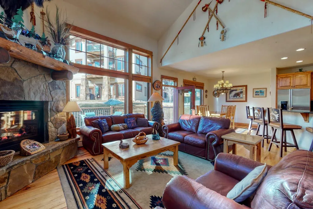 A spacious living room with leather seating, a stone fireplace, and large windows.