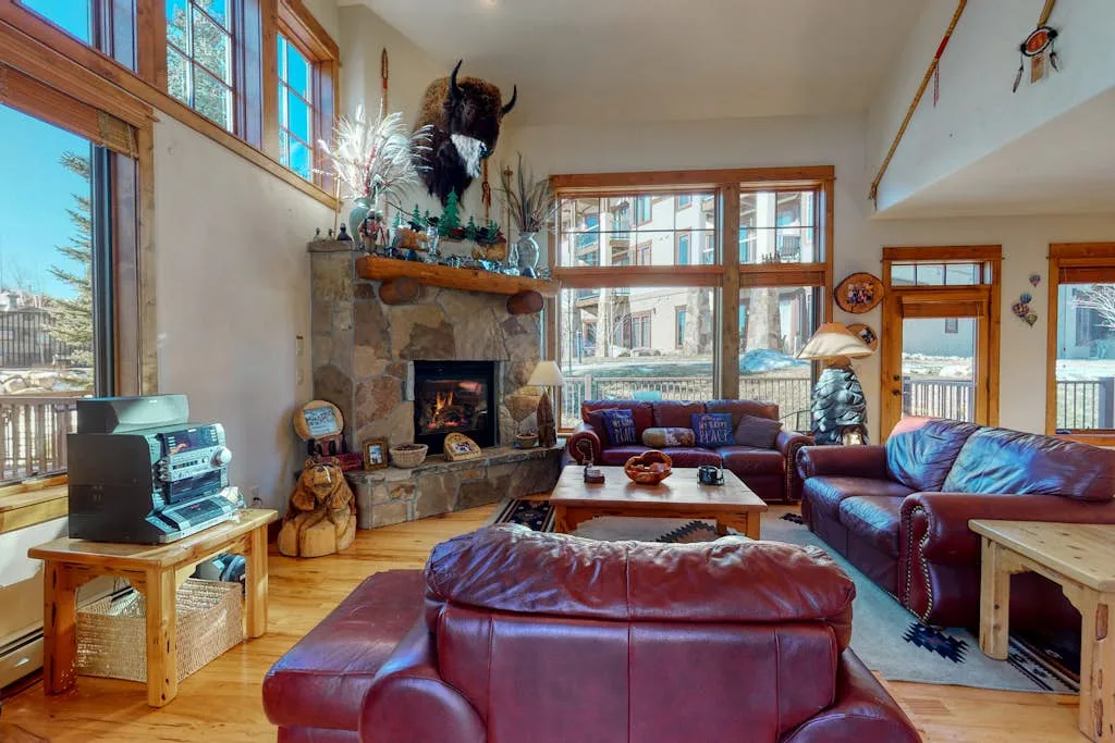 A living room with leather seating, a stone fireplace, and large windows.