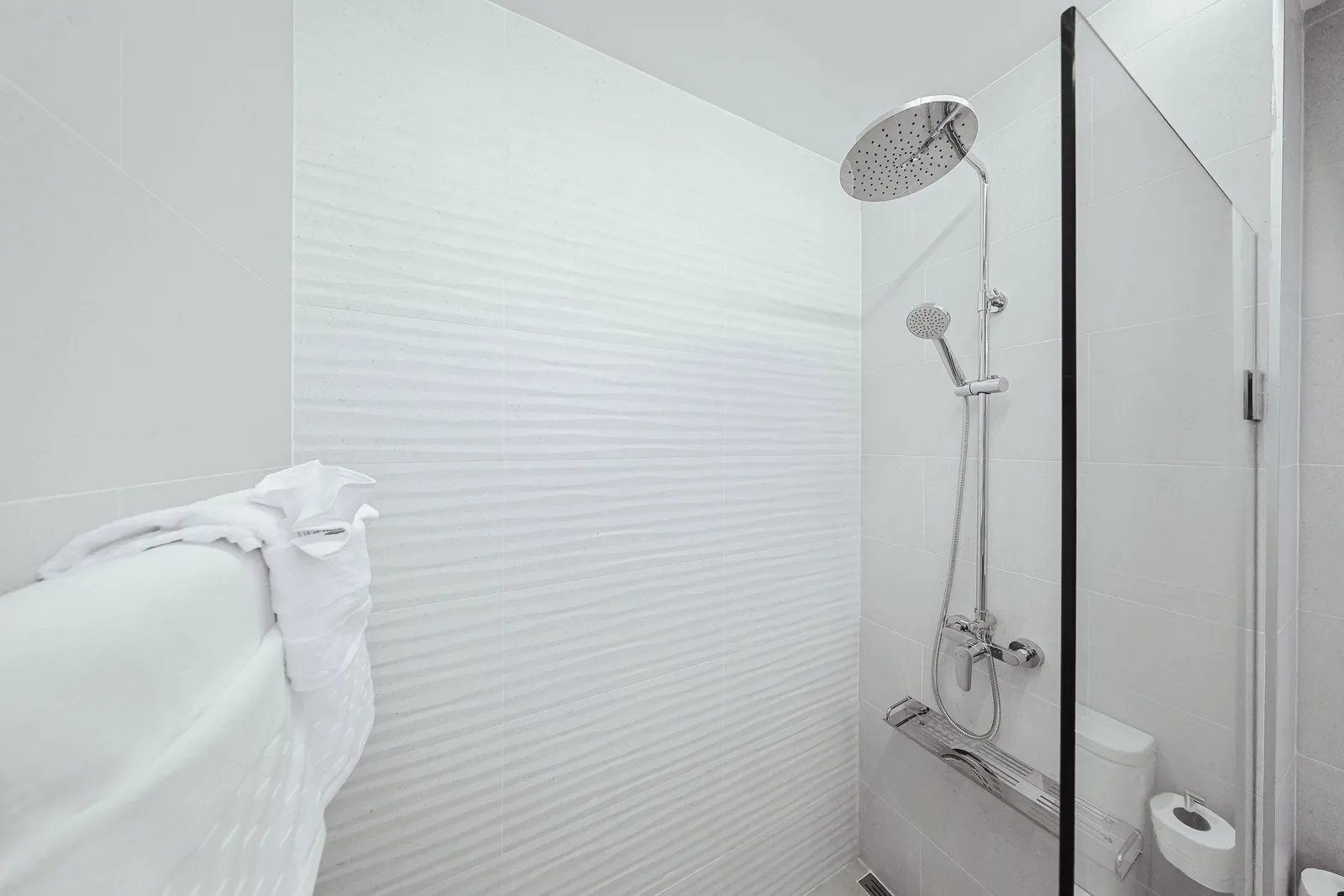 Step into your spotless, modern bathroom featuring a spacious walk-in shower with both rainfall and handheld showerheads. Fresh towels await your arrival in this pristine, bright space.