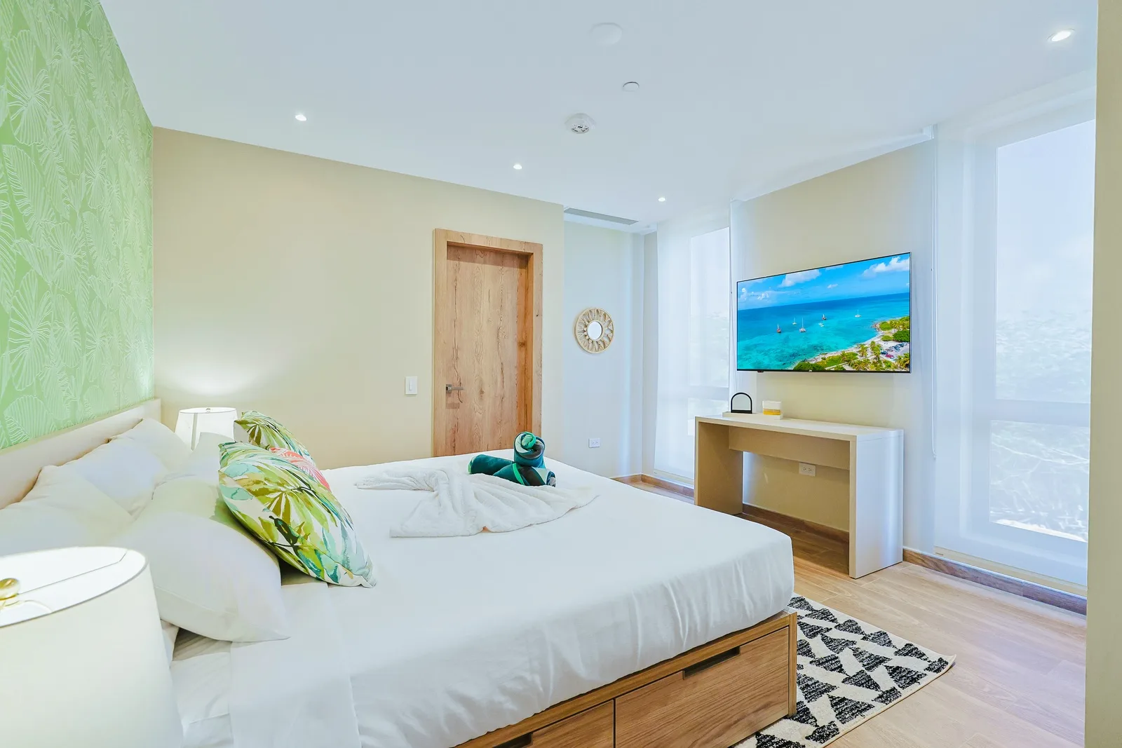 Wake up in your bright coastal bedroom with warm wood tones, tropical touches, and soft natural light streaming through floor-to-ceiling windows.