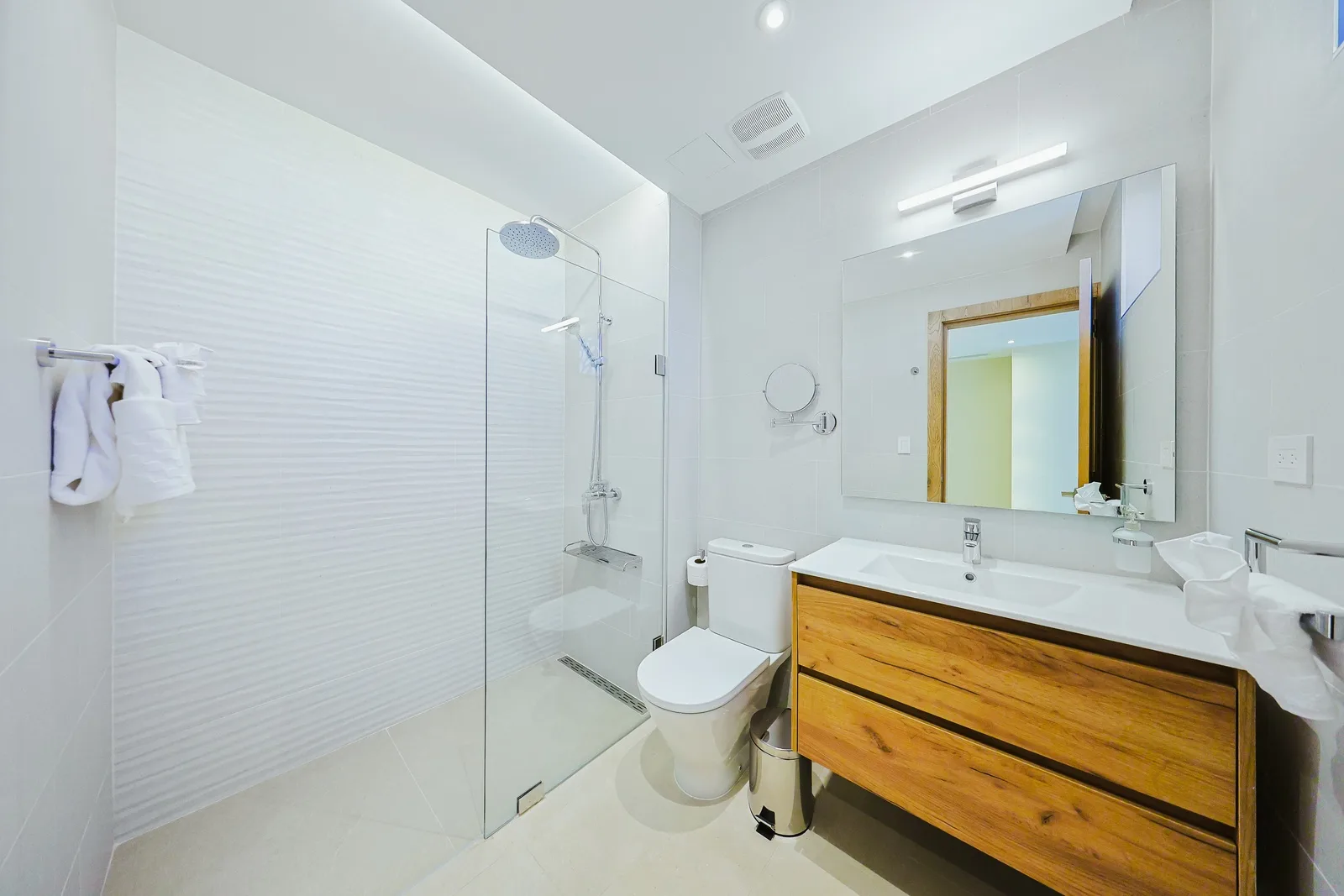 Step into your spa-like bathroom, where clean white tile meets warm wood vanity. Fresh towels await, and the walk-in shower promises a refreshing start to your day.