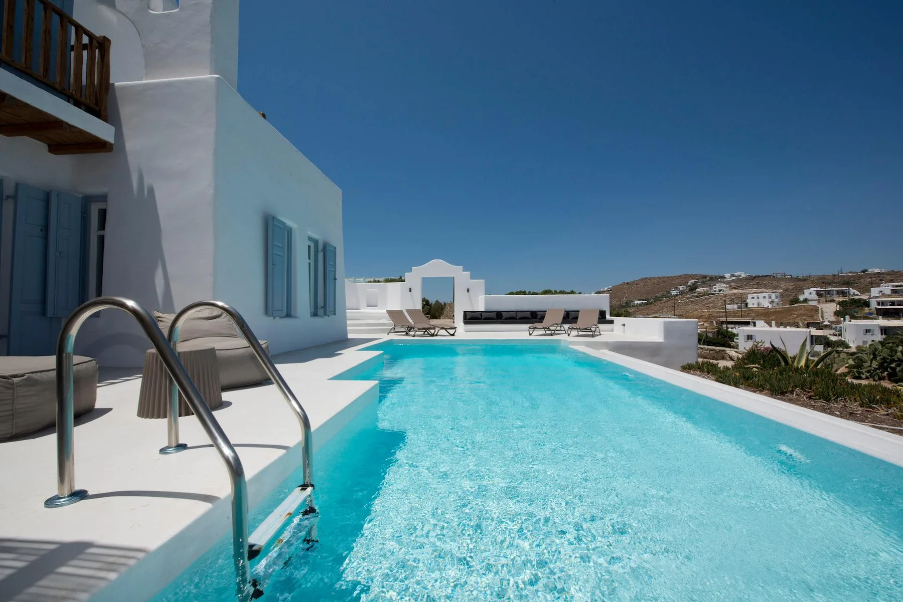 Una piscina al aire libre junto a un edificio blanco, con tumbonas al fondo.
