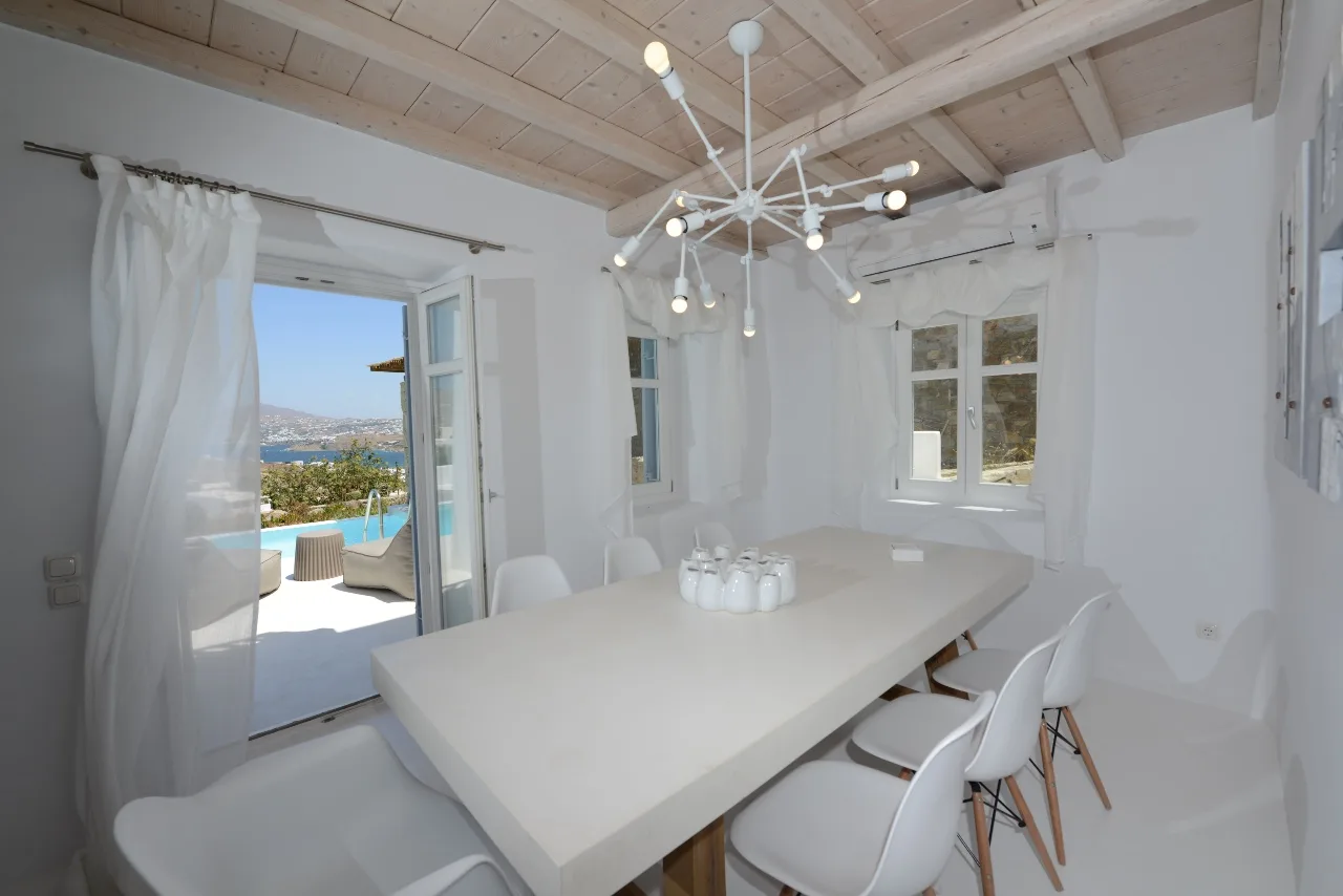 Un comedor luminoso con una mesa blanca larga y una lámpara colgante.