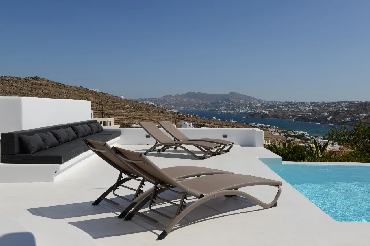 Una terraza soleada junto a la piscina, con tumbonas reclinables y vistas al mar.