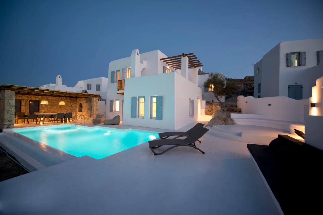 Una villa blanca y una piscina iluminada al anochecer.