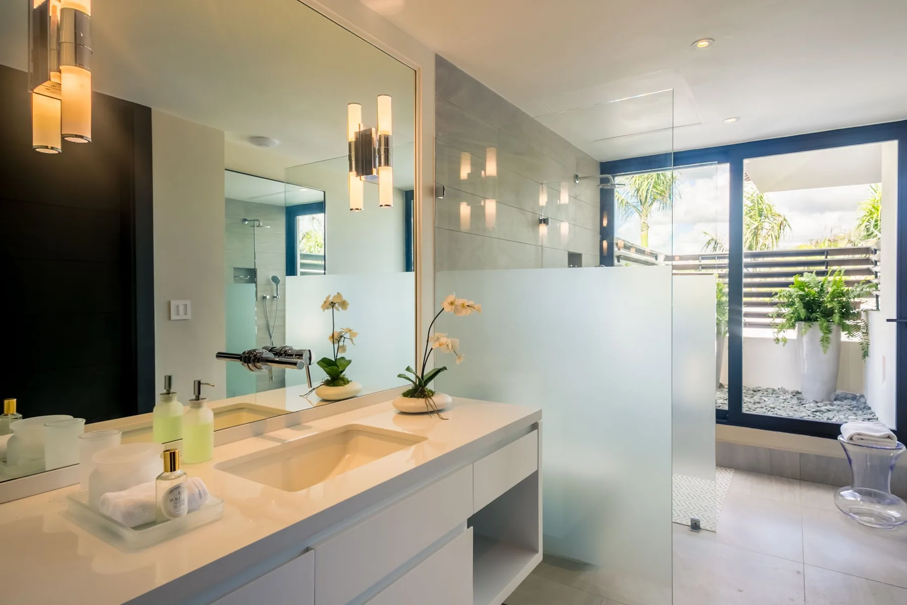 A bright bathroom with a wide vanity, mirror, and glass shower partition.