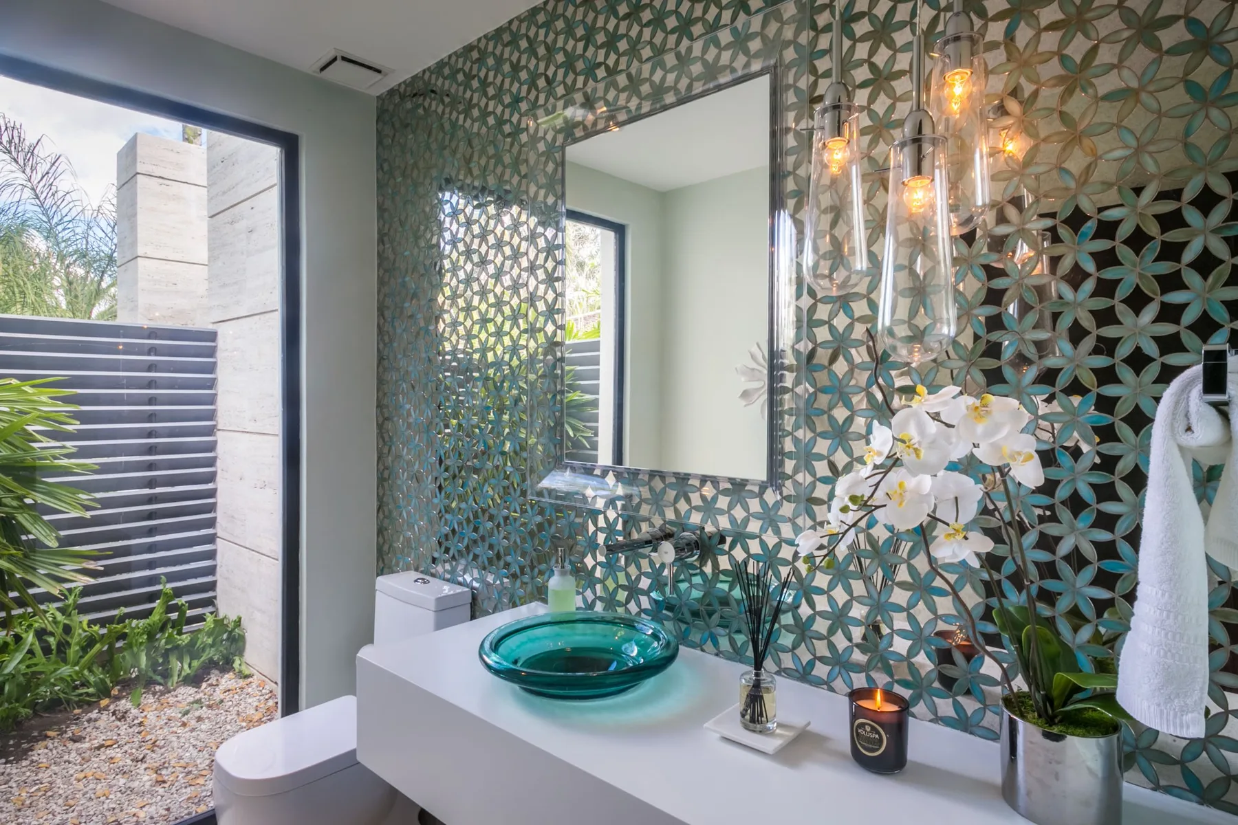 A bathroom vanity with a round glass vessel sink and patterned tile.