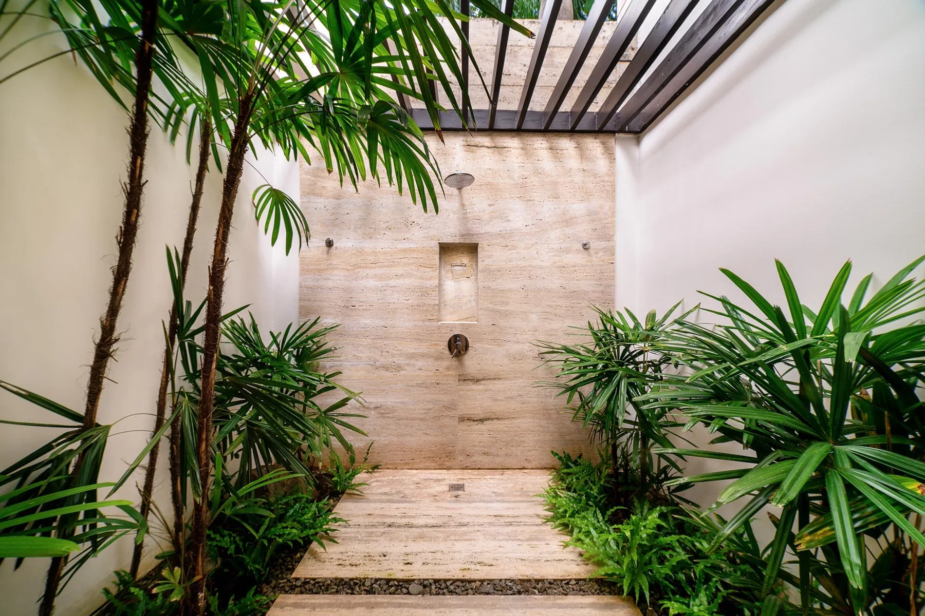 An outdoor shower area with a stone wall and surrounding tropical plants.