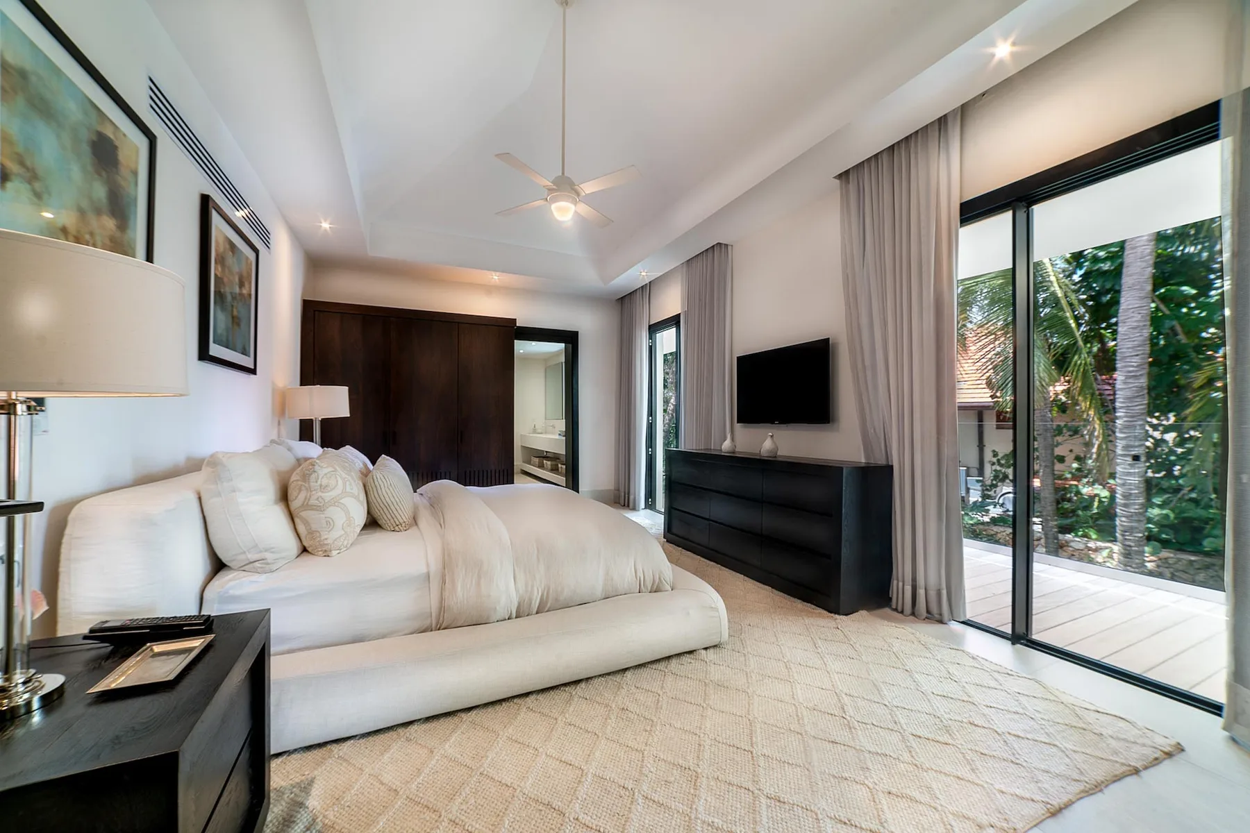 A bedroom with a bed, a television, and sliding glass doors opening to greenery.