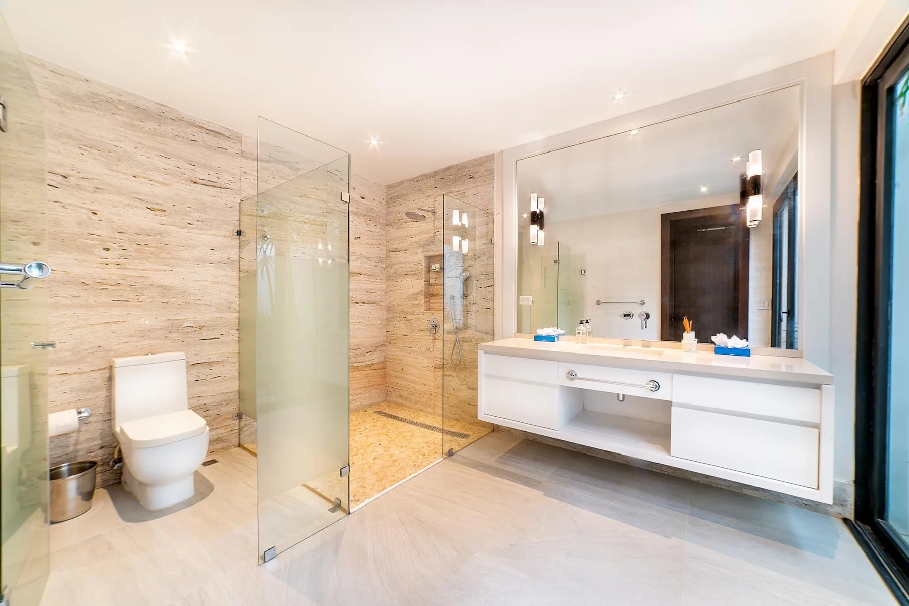 A bright bathroom features a glass shower, a toilet, and a wide vanity.