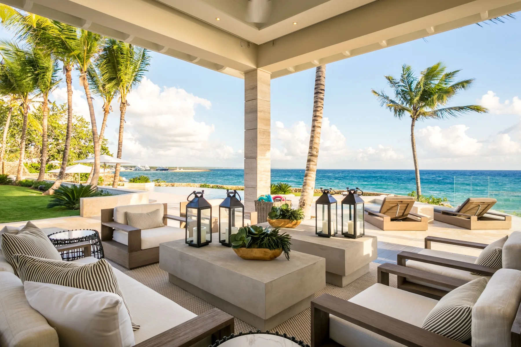 An open-air lounge with cushioned seating overlooks a palm-lined beach and ocean.