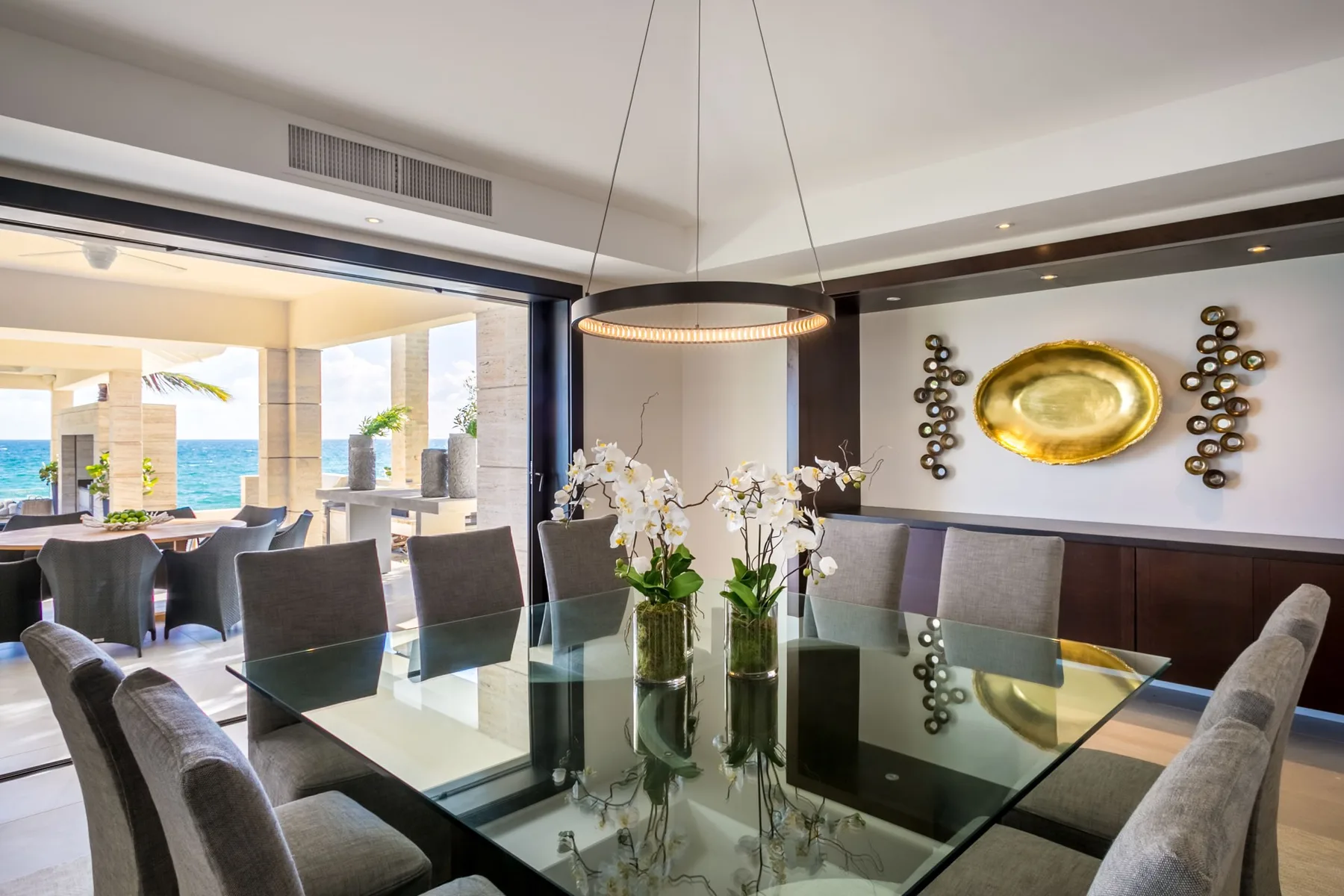A dining area with a glass table, upholstered seating, and floral arrangements.
