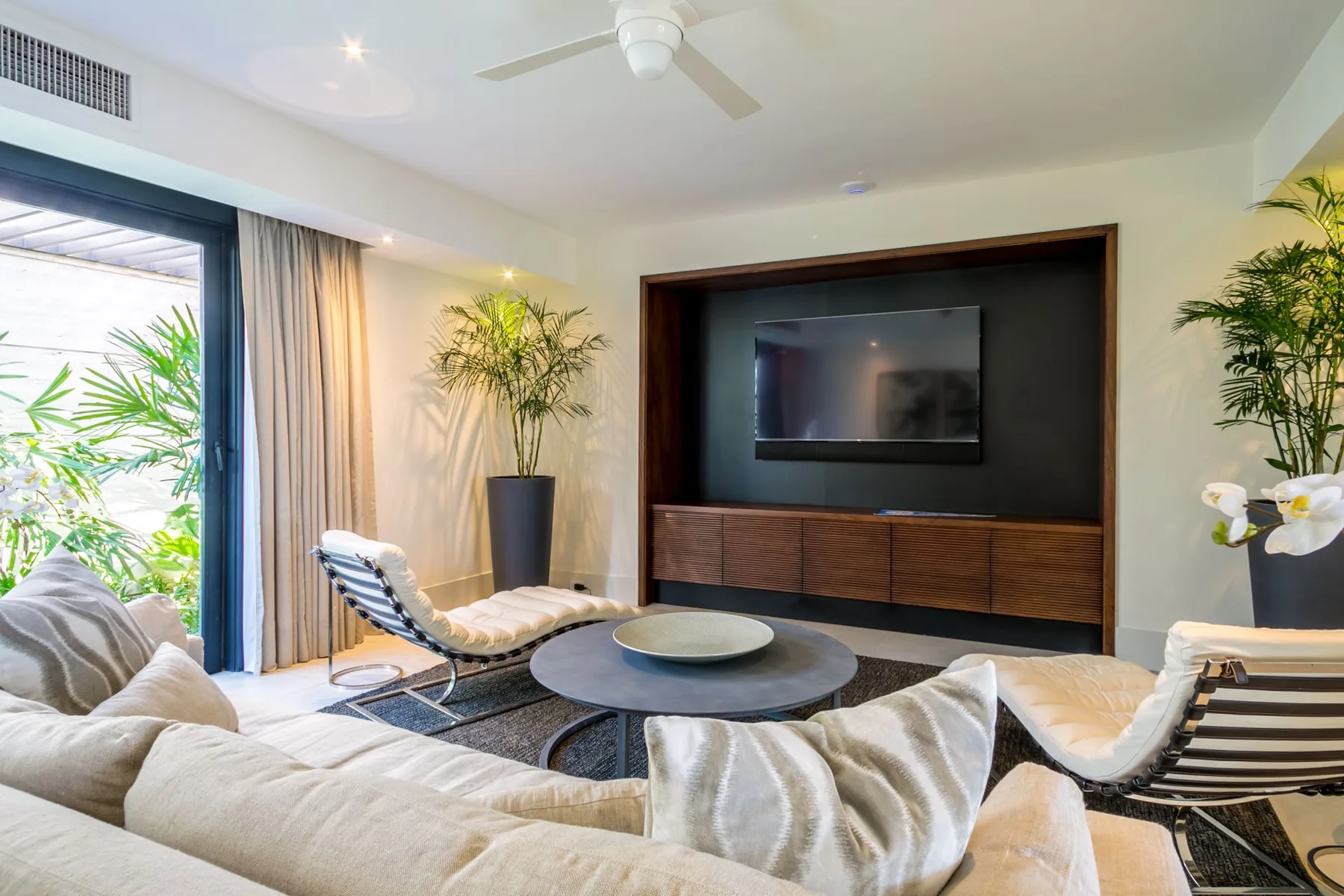 A bright living room with seating around a low table and a wall-mounted television.
