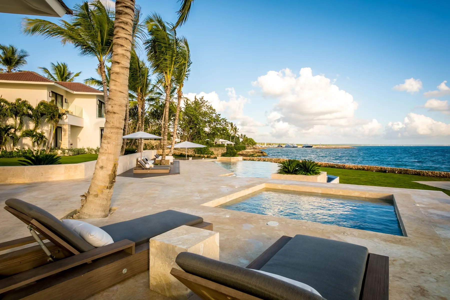 A seaside pool and patio overlook the ocean beside palm trees.