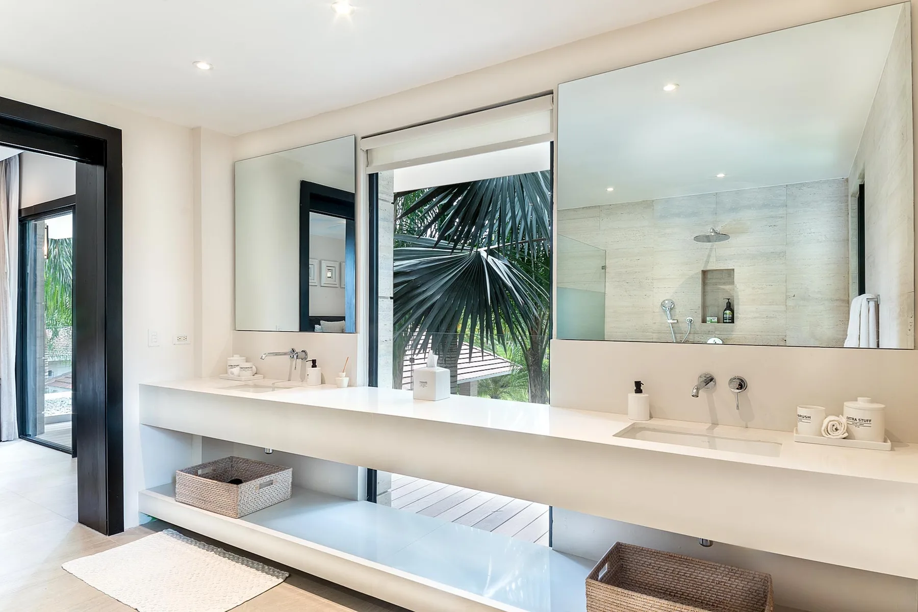 A bright bathroom with a long vanity, wide mirrors, and a shower.