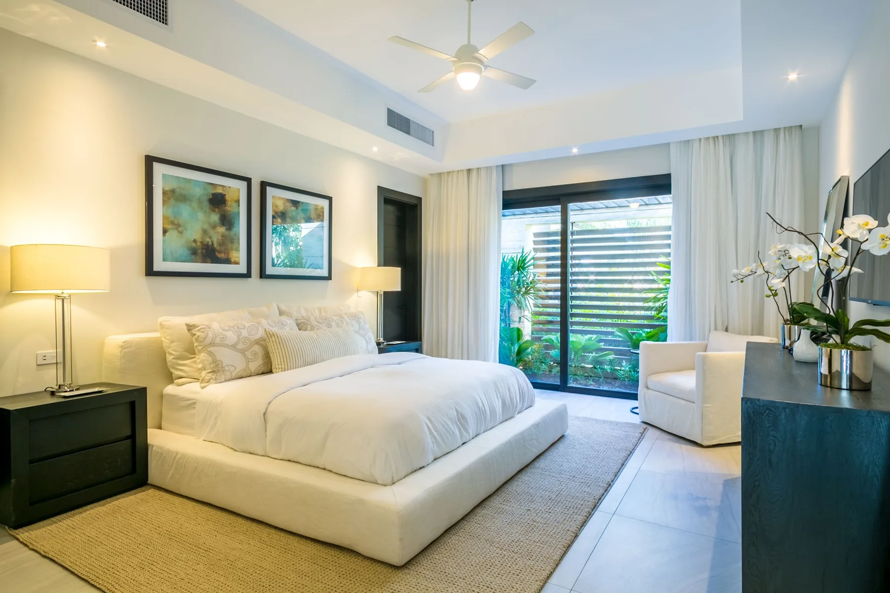 A bright bedroom with a large bed and sliding glass doors opening onto greenery.