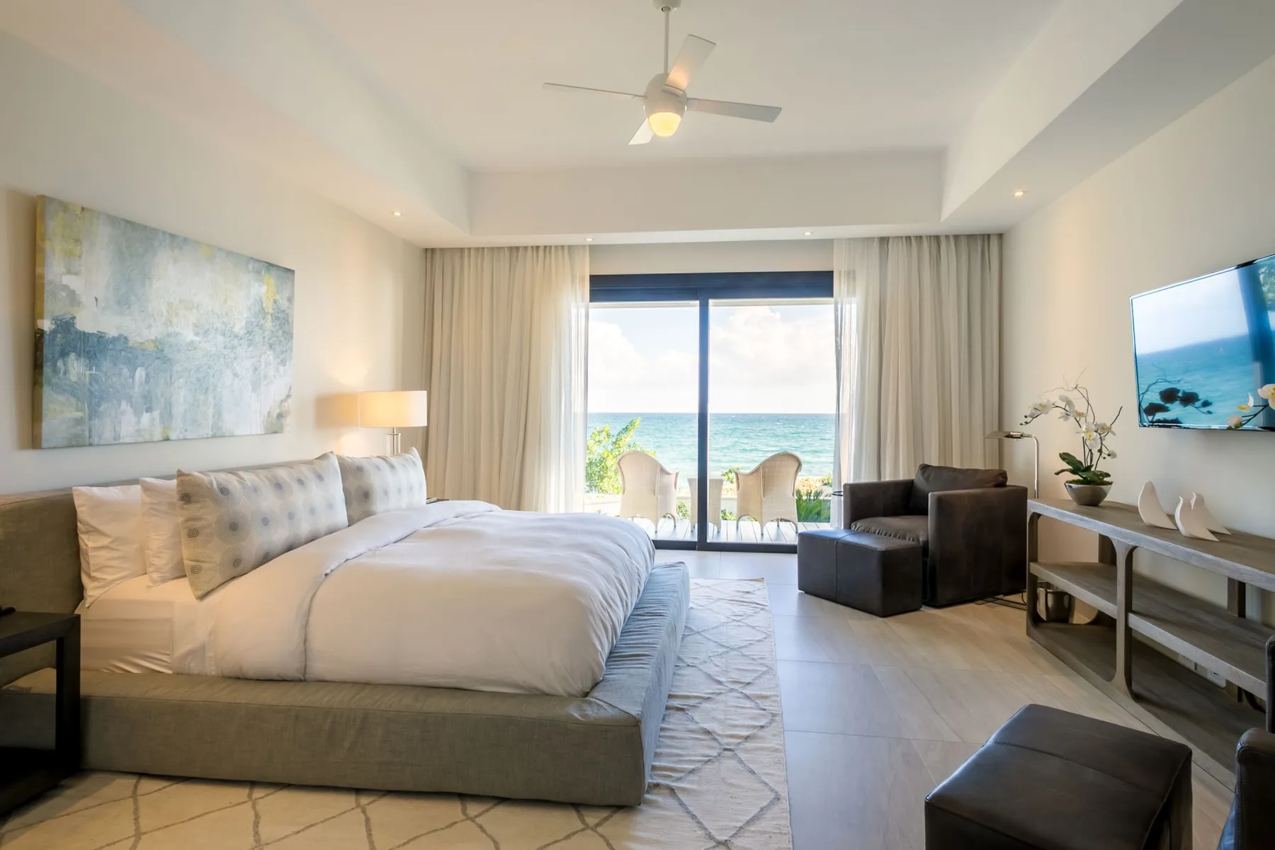 A bright bedroom with a large bed, a seating area, and ocean views through the window.