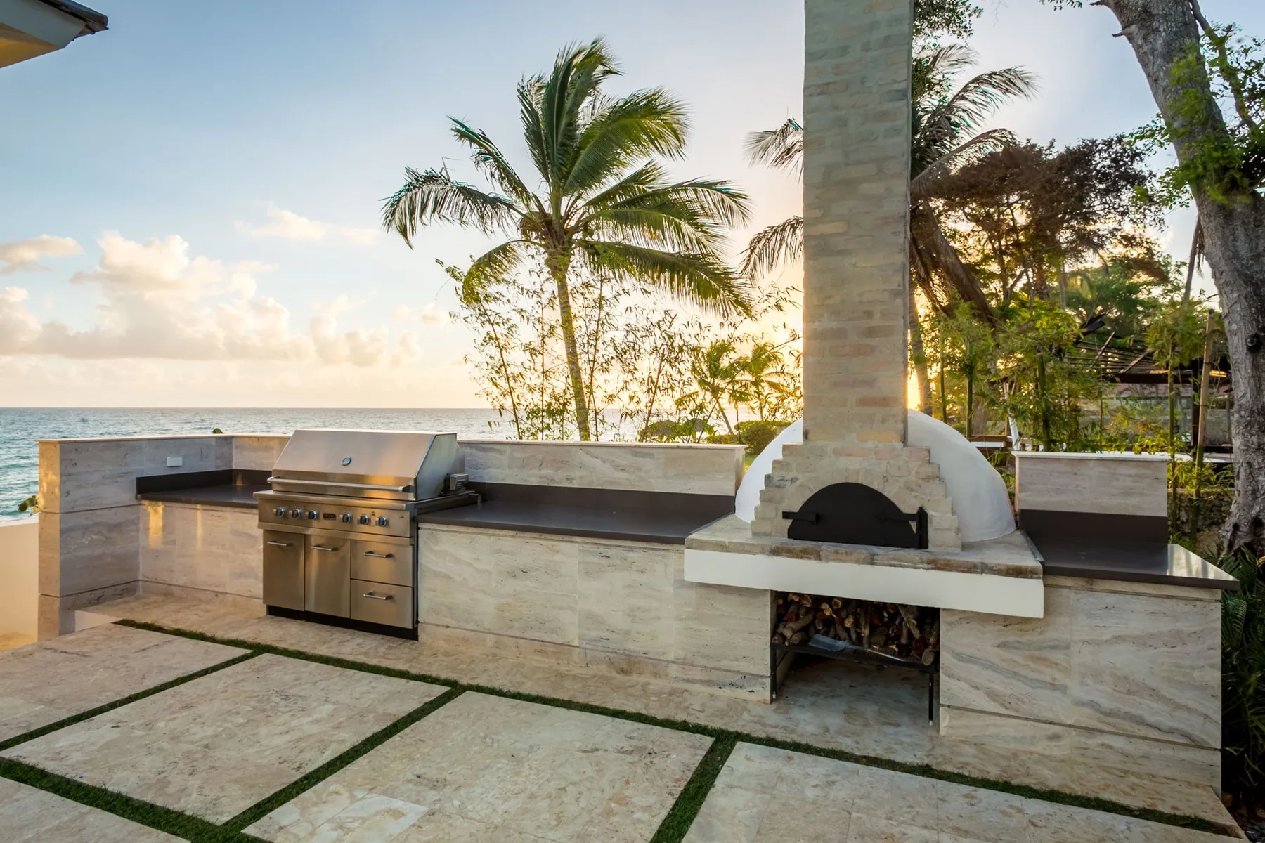 An outdoor cooking area with a built-in grill and oven beside the ocean.