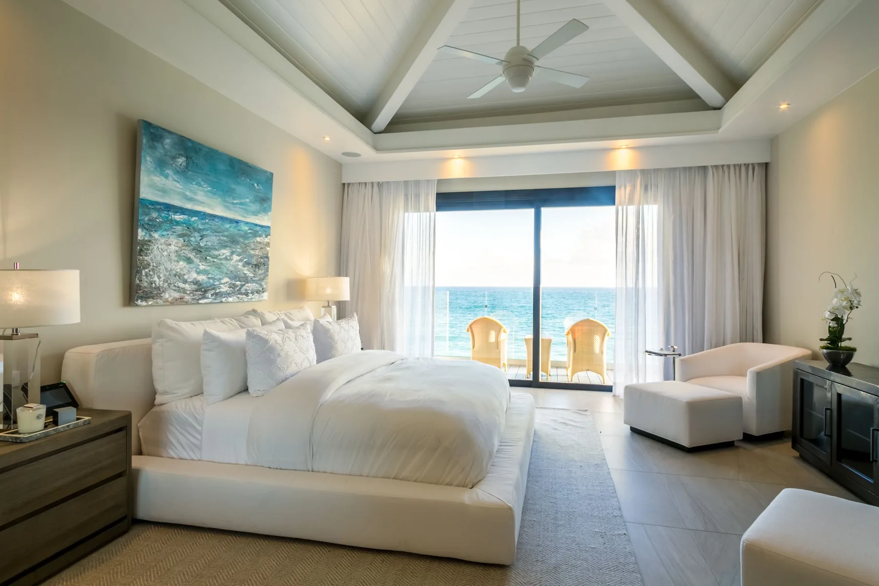 A bright bedroom with a large bed facing a window overlooking the ocean.