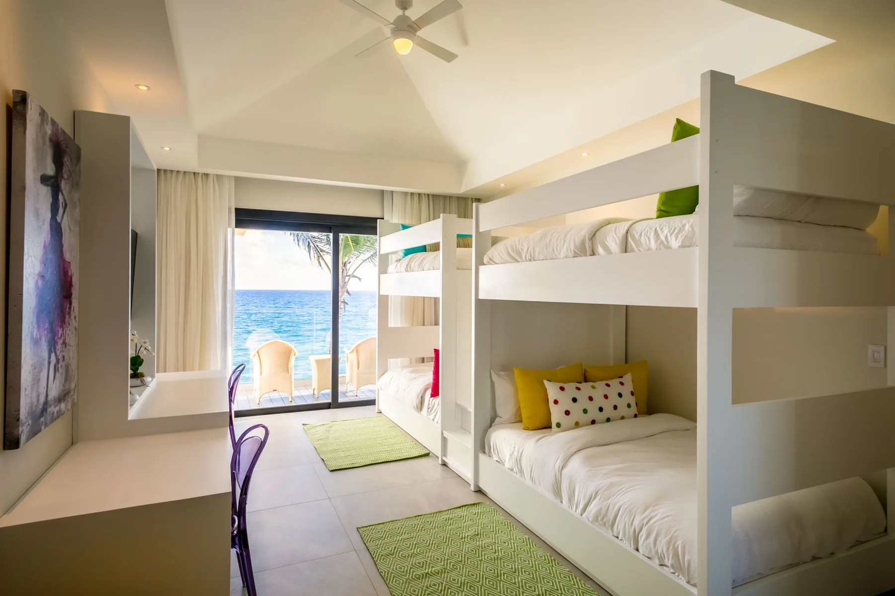 A bright bedroom with white bunk beds and a sliding glass door overlooking the ocean.