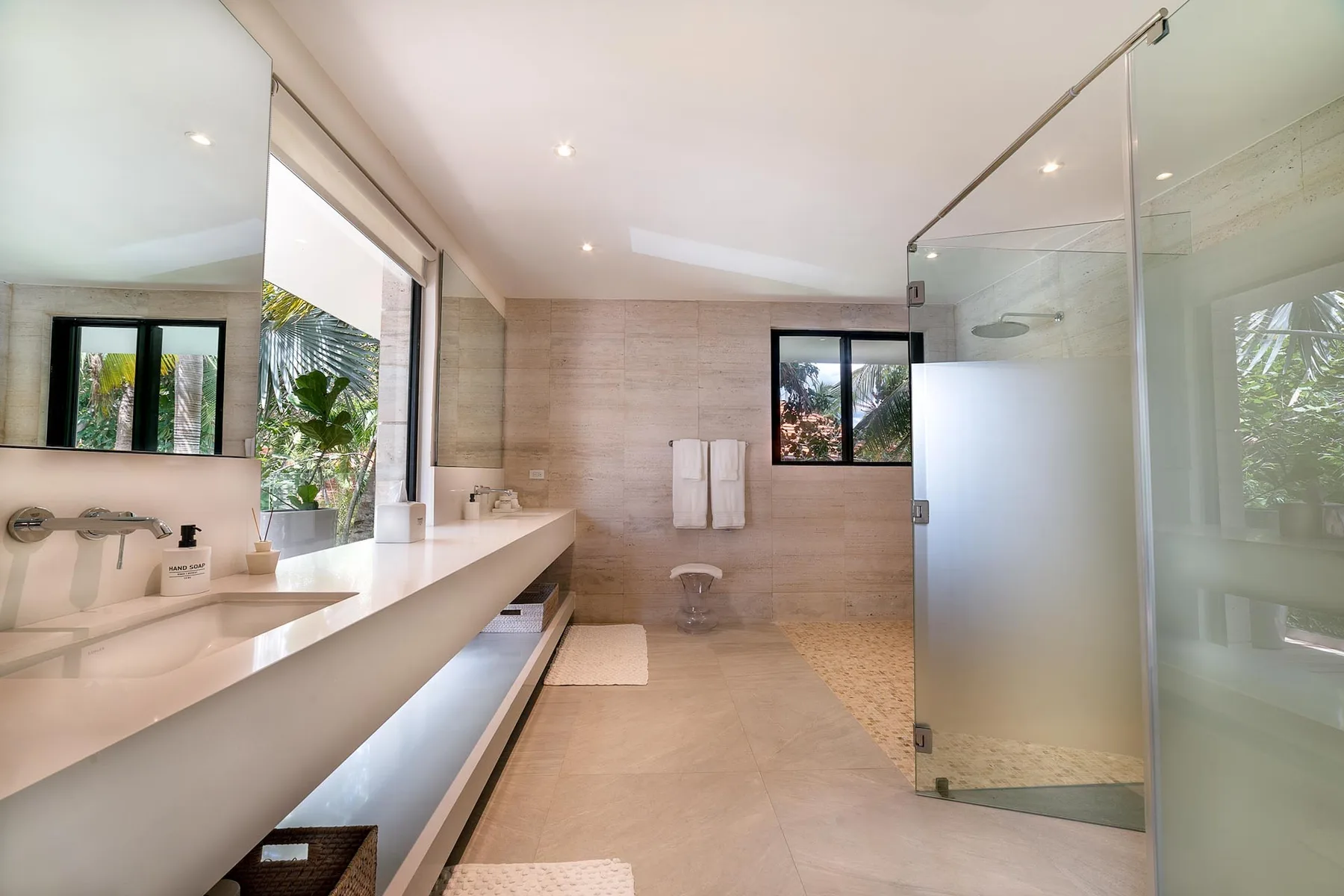 A bright bathroom with a long vanity, wall-mounted towels, and a glass shower.