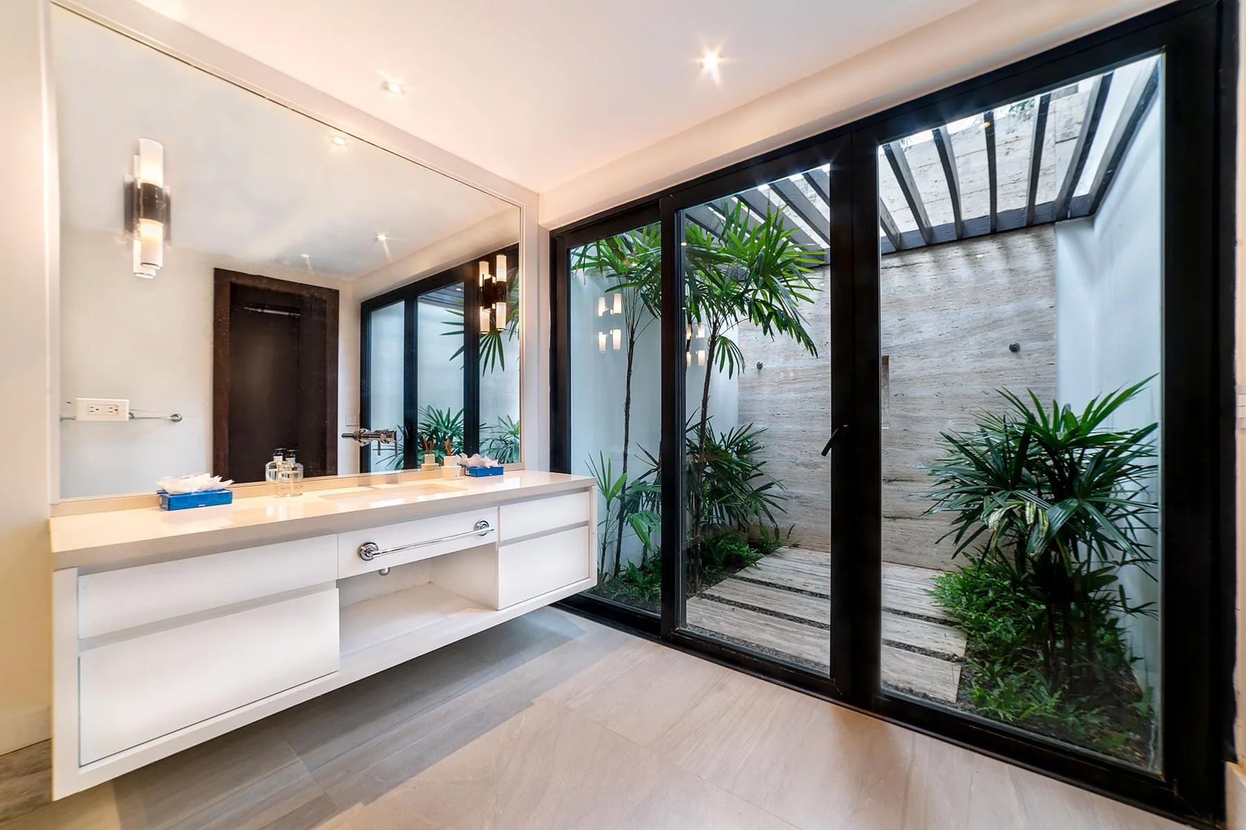A bathroom vanity faces large glass doors opening onto a small planted courtyard.
