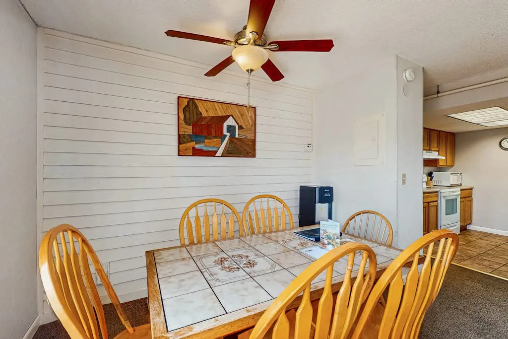 A dining area with a tiled table and wooden seating beneath a ceiling fan.