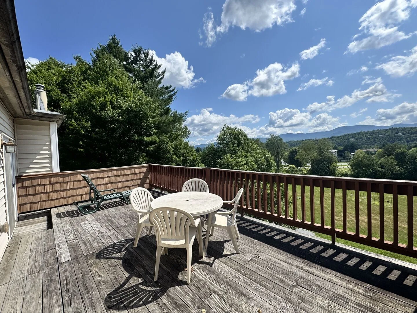 A wooden deck with outdoor seating overlooks green hills beneath a sunny sky.