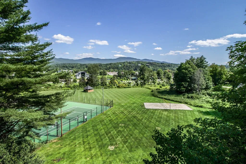 An outdoor tennis court and broad green lawn sit beneath a clear sky.