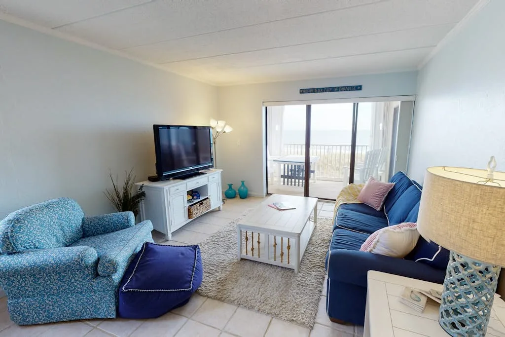 A living room with blue seating, a television, and sliding glass doors opening to a balcony.