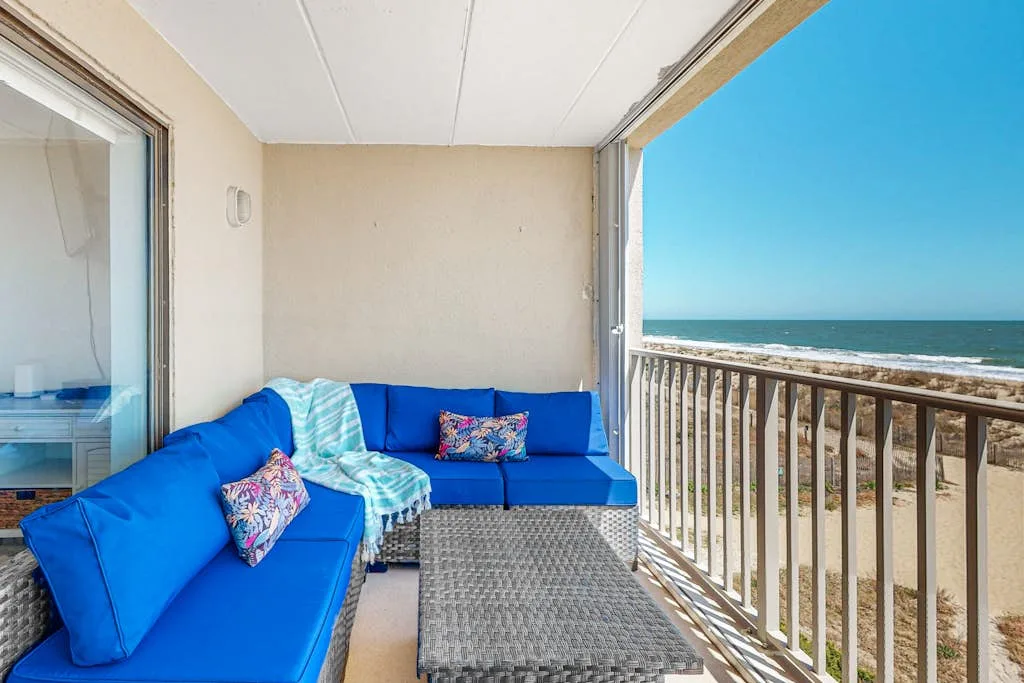 A balcony seating area with blue cushions overlooks the ocean.