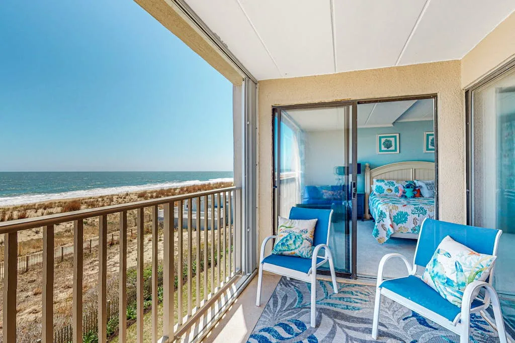 A covered balcony overlooks the ocean, with blue seating beside an open sliding glass door.